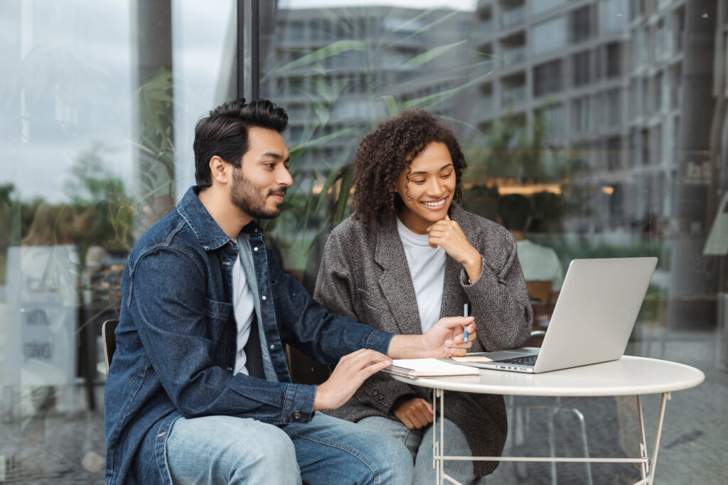 Dois colegas sorrindo diante de um notebook em mesa de trabalho